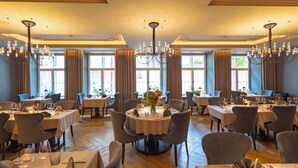 Un espace repas avec des tables rondes, des chaises, des lustres et de grandes fenêtres ornées de rideaux.