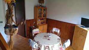 A dining area with a round table, chairs, a wooden cabinet, and a hanging plant.