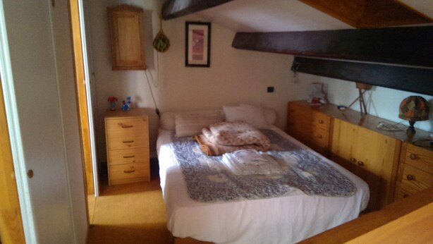 A bedroom with a bed, a wooden dresser, a nightstand, and a ceiling fan.