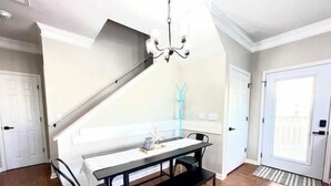 A dining area with a black table, two black chairs, a bench, a chandelier, and a view of a balcony. - Sea Breeze Retreat with Gorgeous Ocean Views! (Myrtle Beach)