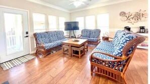A spacious living room with a wooden floor, a ceiling fan, and a large window. - Sea Breeze Retreat with Gorgeous Ocean Views! (Myrtle Beach)