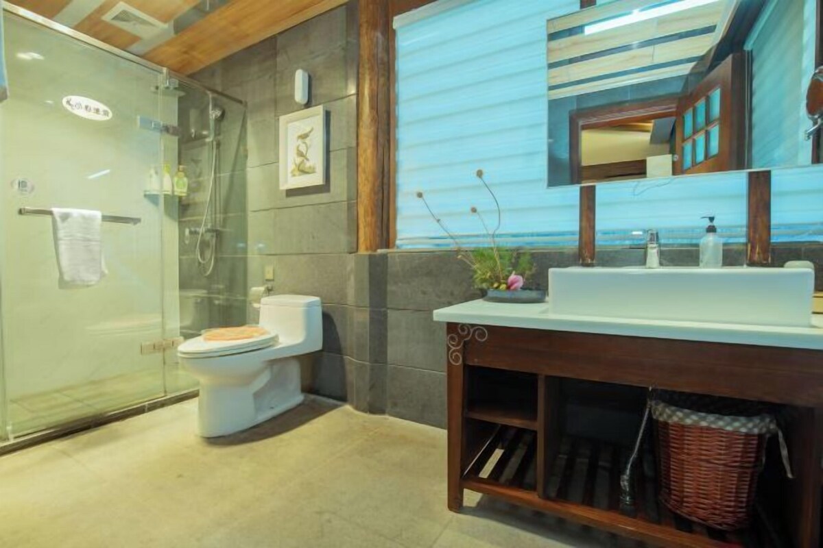 A modern bathroom with a glass shower enclosure, a white toilet, a wooden vanity with a sink, and a mirror.