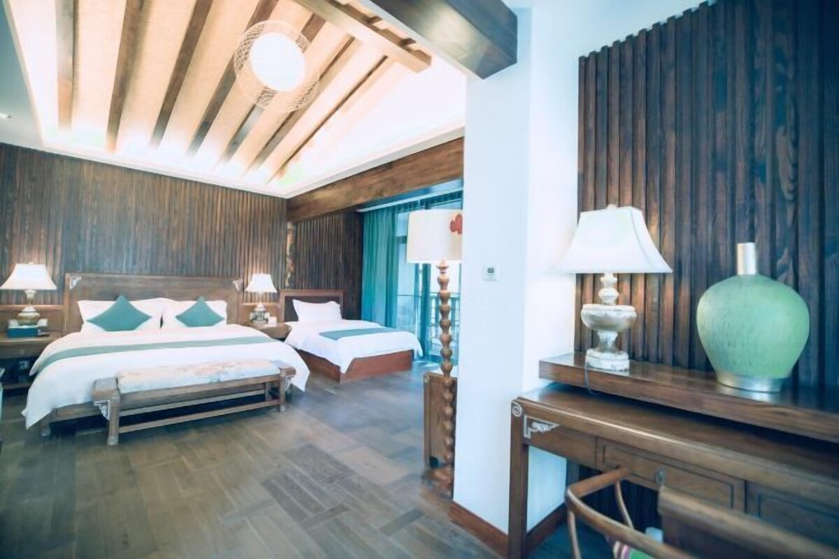 A hotel room with a wooden ceiling, two beds, a desk, and a large window.