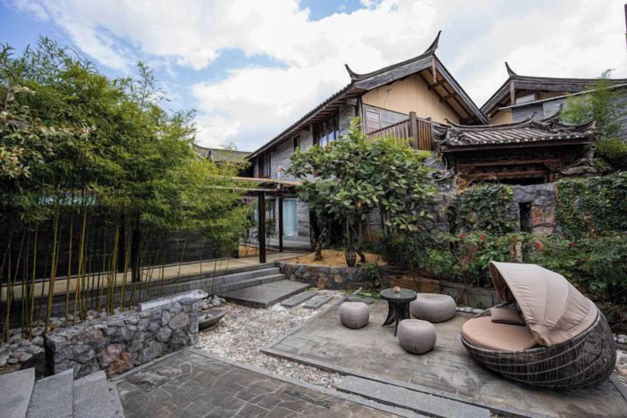 A traditional Japanese-style courtyard with stone lanterns, a bamboo fence, and a seating area with cushions.