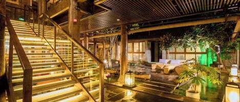 Una escalera con escalones iluminados, techo de madera y una zona de estar con plantas y faroles.