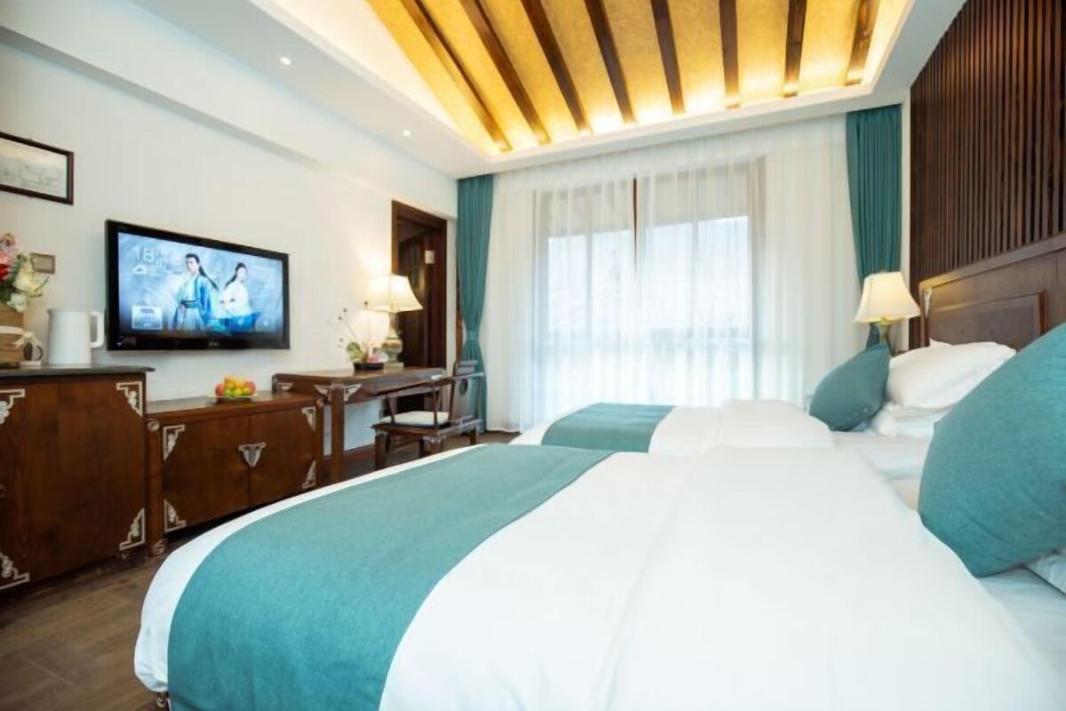A hotel room with two beds, a TV, a desk, and a window with curtains.