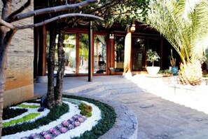 A pathway leading to a building with a covered entrance, surrounded by a landscaped garden with a circular flower bed and palm trees. - Shuhe Yuannian Holiday Courtyard (Lijiang)