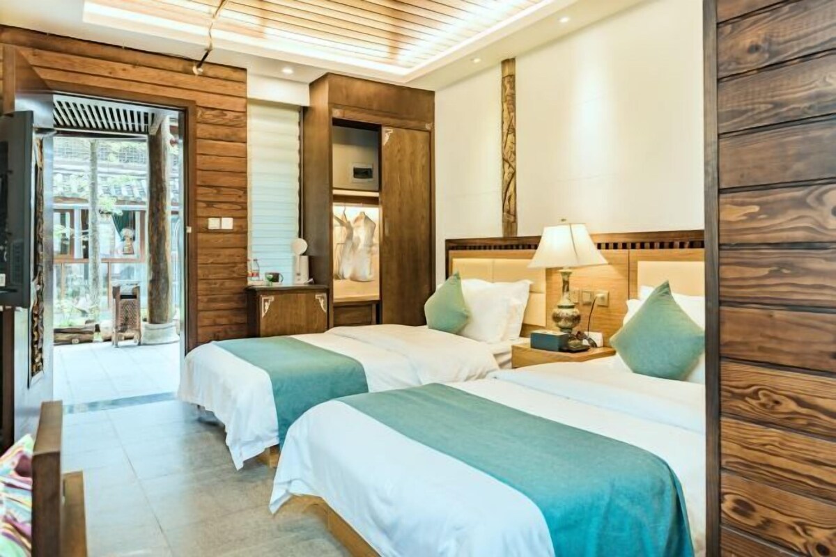 A hotel room with two beds, wooden paneling, a nightstand with a lamp, and a view of the outside.