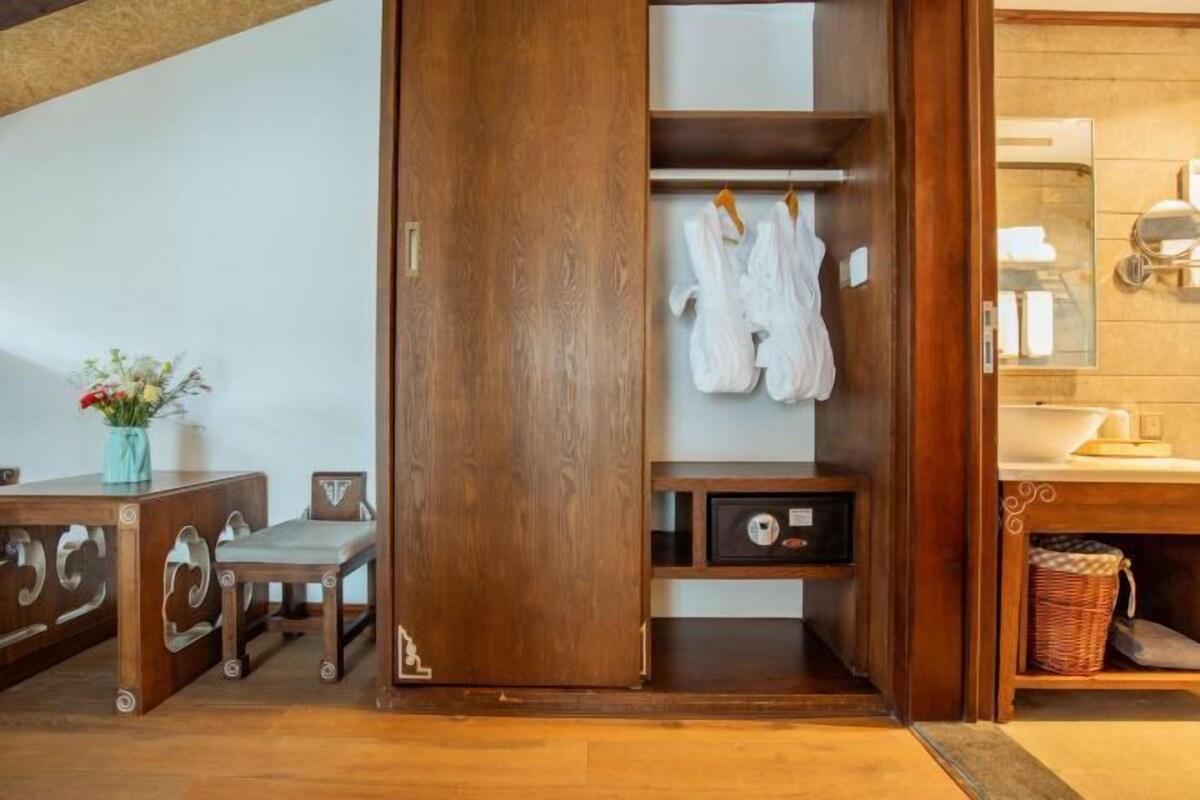 A wooden wardrobe with a mirror, a small bench, and a hanging rack with white robes.