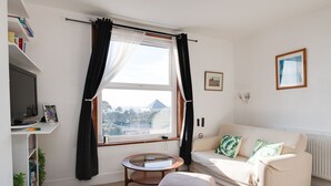 A living room with a sofa, a round table, a television, and a window with curtains.