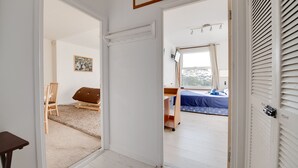 A hallway leading to a bedroom with a bed, a chair, and a small table.