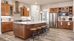 A modern kitchen with wooden cabinets, a large island with stools, stainless steel appliances, and pendant lighting. - Outdoor Sanctuary/Lake View/Hot tub & Game Room! (Canyon Lake)