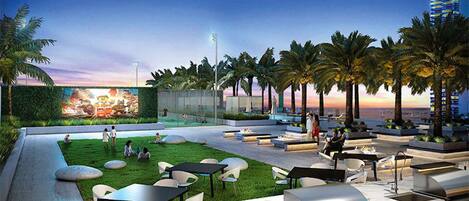 An outdoor dining area with tables and chairs, palm trees, and a view of the city skyline.