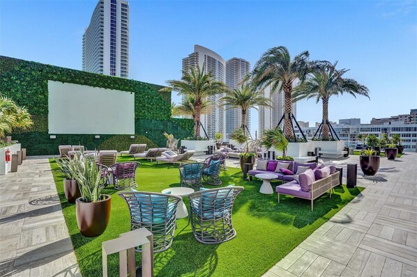 Un lounge en la azotea con asientos al aire libre, palmeras y vistas a edificios altos.