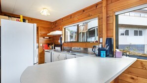 A kitchen with wooden walls, a white refrigerator, a sink, and a window with a view of a house. - Crystal Clear - Snells Beach Holiday Home (Snells Beach)