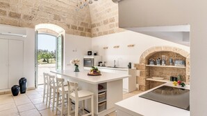 Une cuisine moderne avec un mur en pierre, des meubles blancs et un îlot central doté de sièges.
