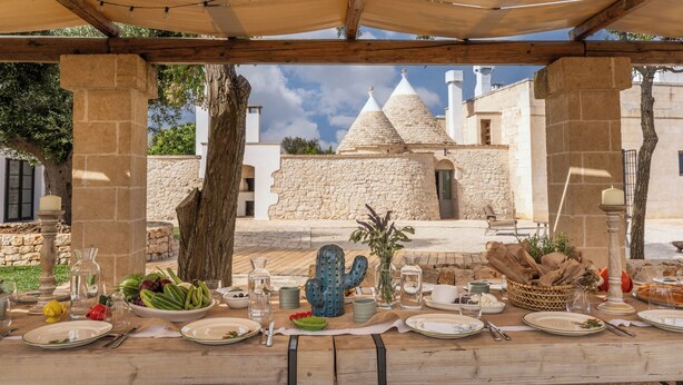 Un espace de restauration en plein air avec une table dressée pour un repas, une décoration en forme de cactus et un bâtiment en pierre en arrière-plan.