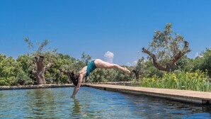 Une personne effectuant un saut arrière et atterrissant dans une piscine entourée d’arbres et de verdure.