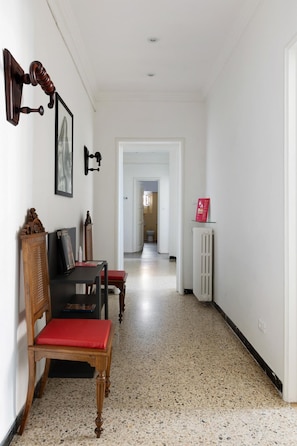 Um corredor com uma cadeira de madeira e uma pequena mesa, um radiador e uma porta que dá para outro quarto.