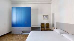 Un dormitori amb un llit gran, un armari blau, dues cadires, una taula petita i un quadre encimbellat a la paret.