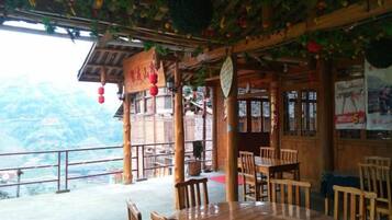 A wooden dining area with tables and chairs, a balcony with a view of the mountains, and traditional Chinese decorations.