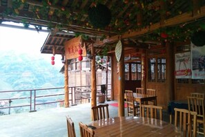 Una zona de menjador de fusta amb taules i cadires, un balcó amb vista a les muntanyes i decoracions tradicionals xineses.
