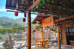 Una estructura de madera tradicional con un letrero, asientos al aire libre y vistas a las montañas.