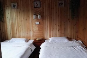 A wooden room with two beds, a small table with a bowl, and framed pictures on the wall. - Juyou Hostel (Longsheng)