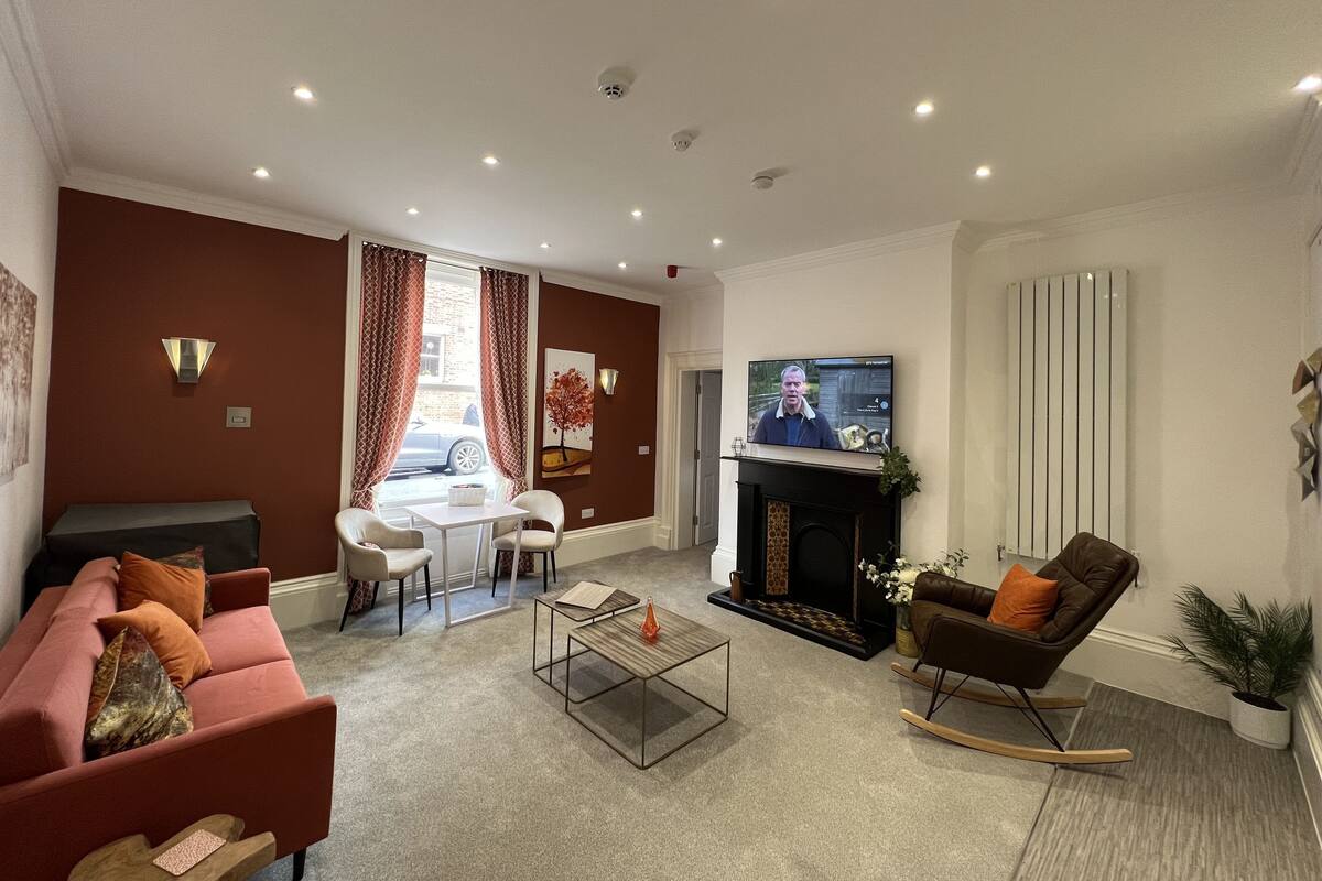 A modern living room with a sofa, a coffee table, a fireplace, a TV, and a dining area.