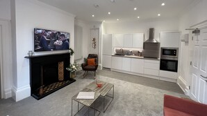 A modern living room with a fireplace, a television, a coffee table, and a red chair. - Winckley Square Residences (Preston)