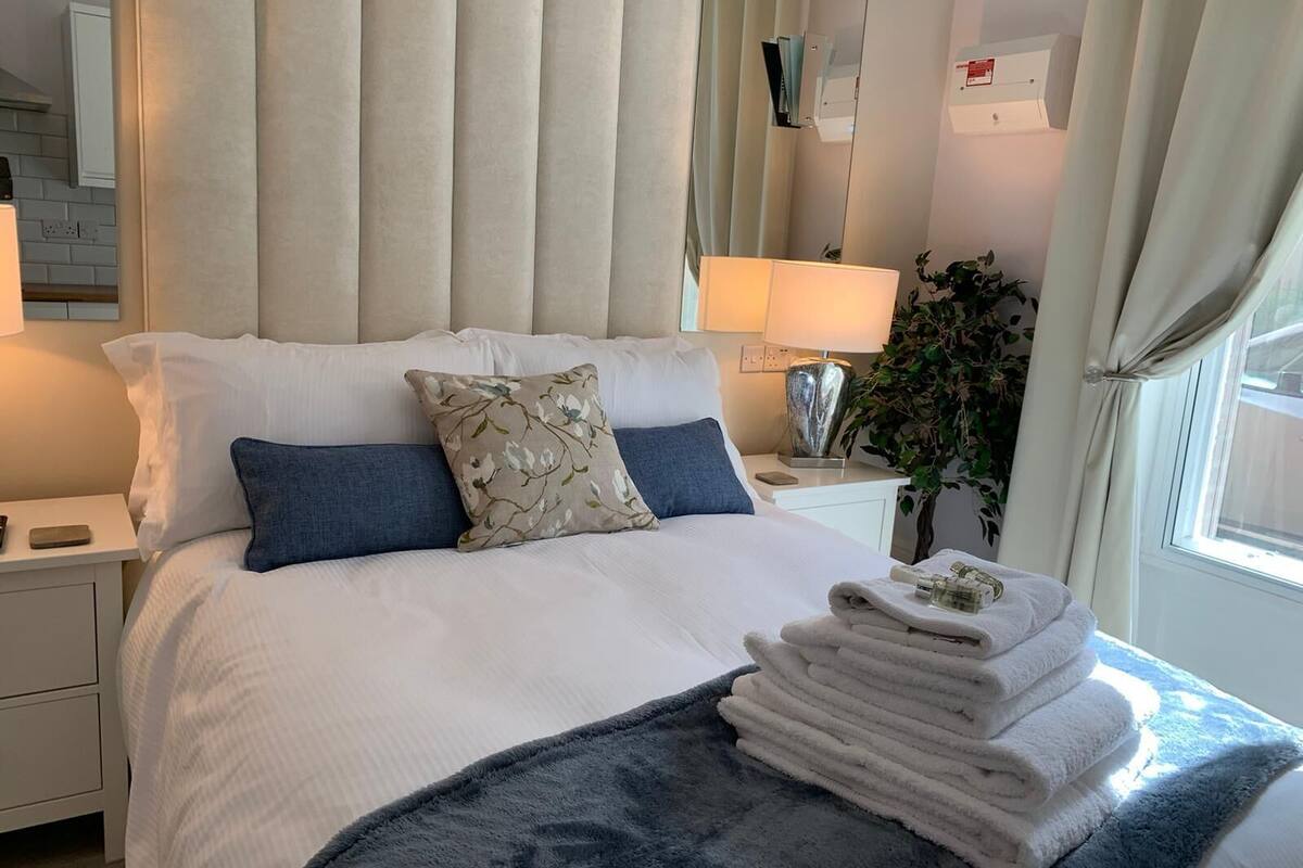 A neatly made bed with white linens, a blue throw blanket, and a stack of white towels.