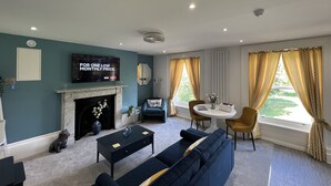 A living room with a fireplace, a TV mounted on the wall, a sofa, a coffee table, and a dining area with a table and chairs. - Winckley Square Residences (Preston)