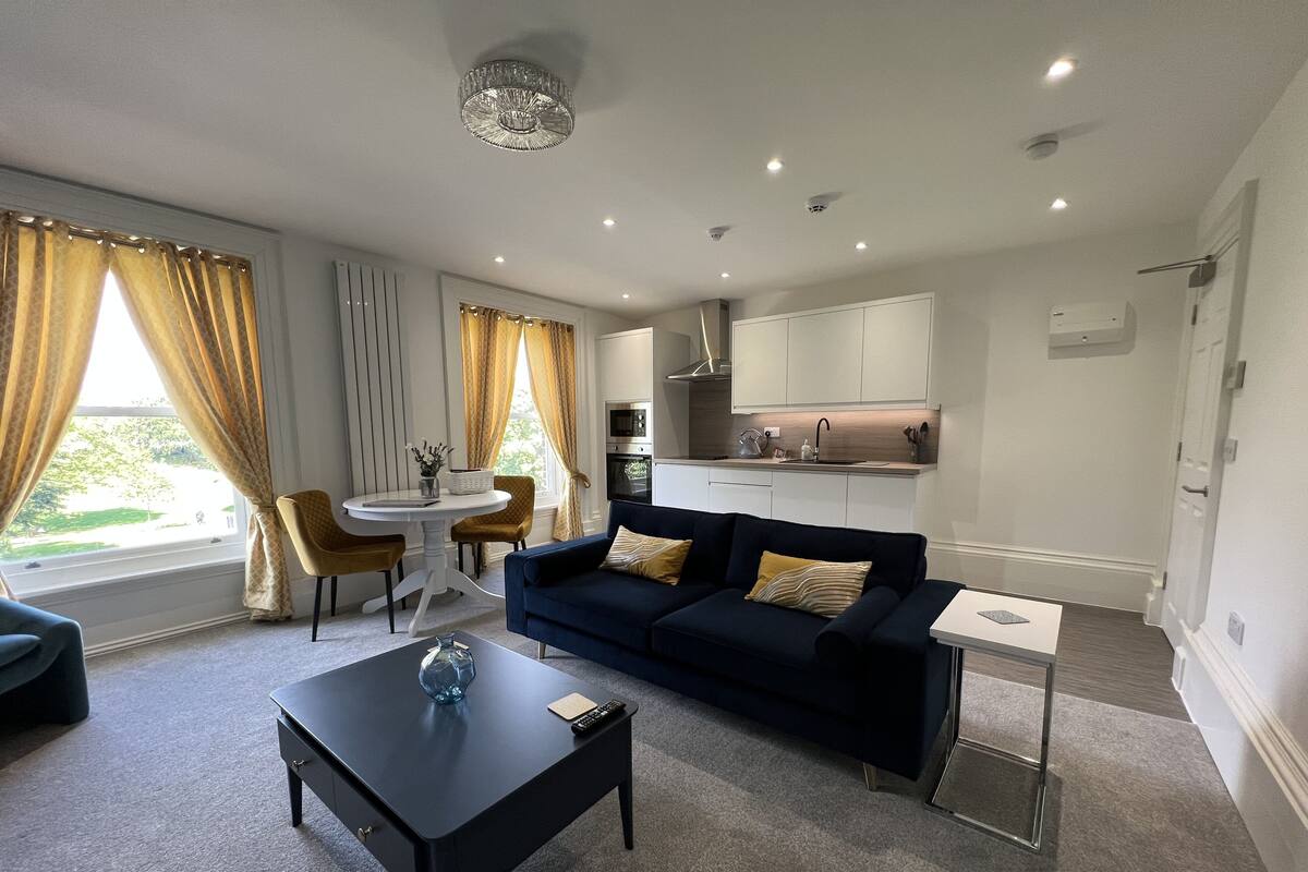 A modern living room with a dark blue sofa, a coffee table, and a dining area with a white table and chairs.