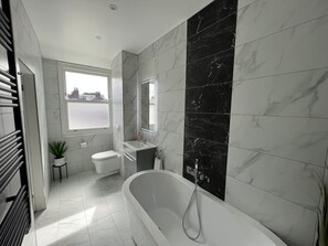 Ein modernes Badezimmer mit freistehender Badewanne, Toilette, Waschbecken und einem Fenster mit Blick.
