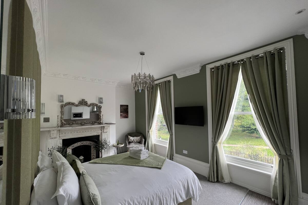A bedroom with a large bed, a fireplace, a television, and a view of the outdoors.