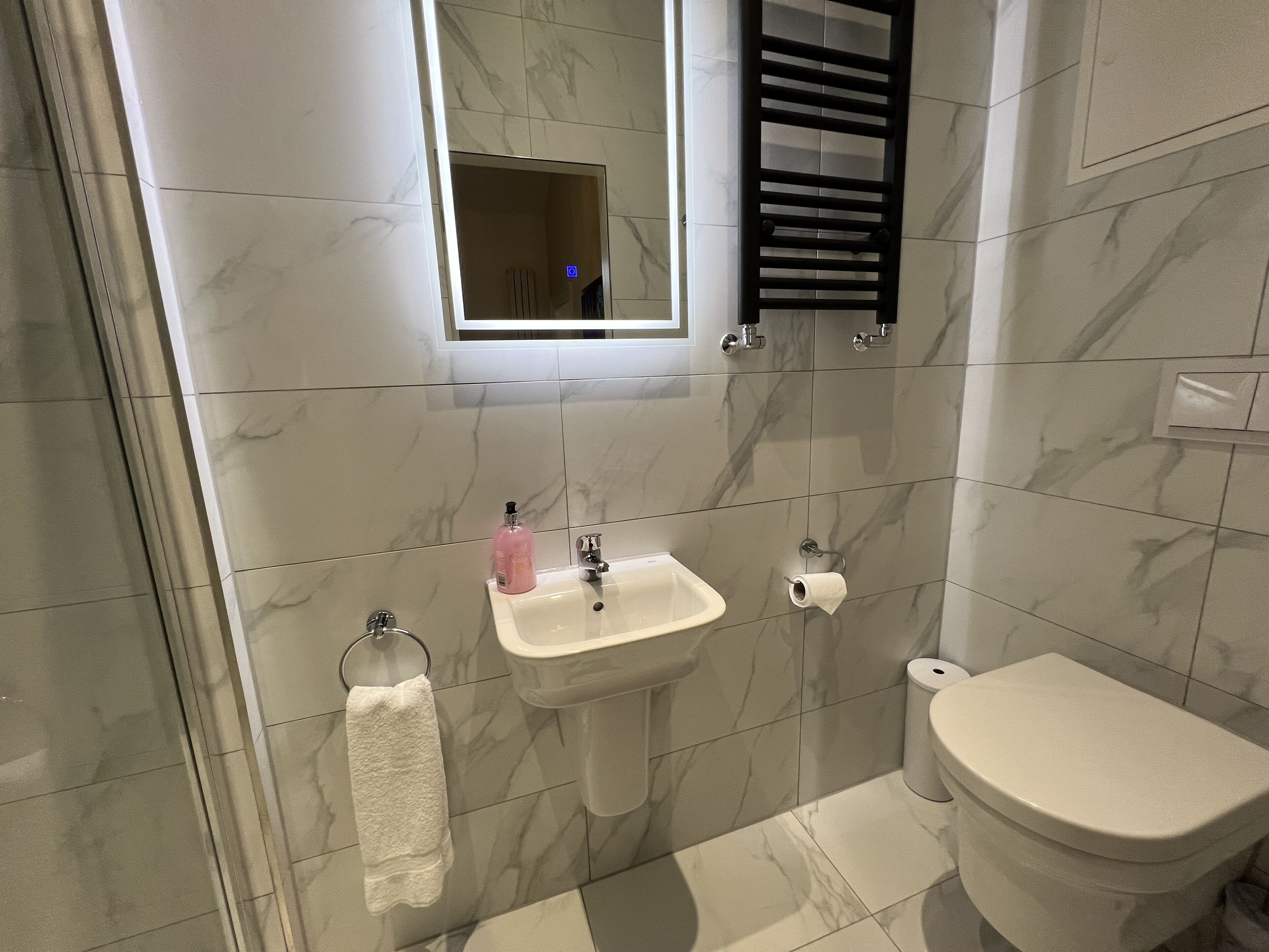 A bathroom with a marble-tiled wall, a white sink, a toilet, and a towel rack.