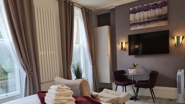 A hotel room with a bed, a desk, two chairs, a TV, and a radiator. - Winckley Square Residences (Preston)