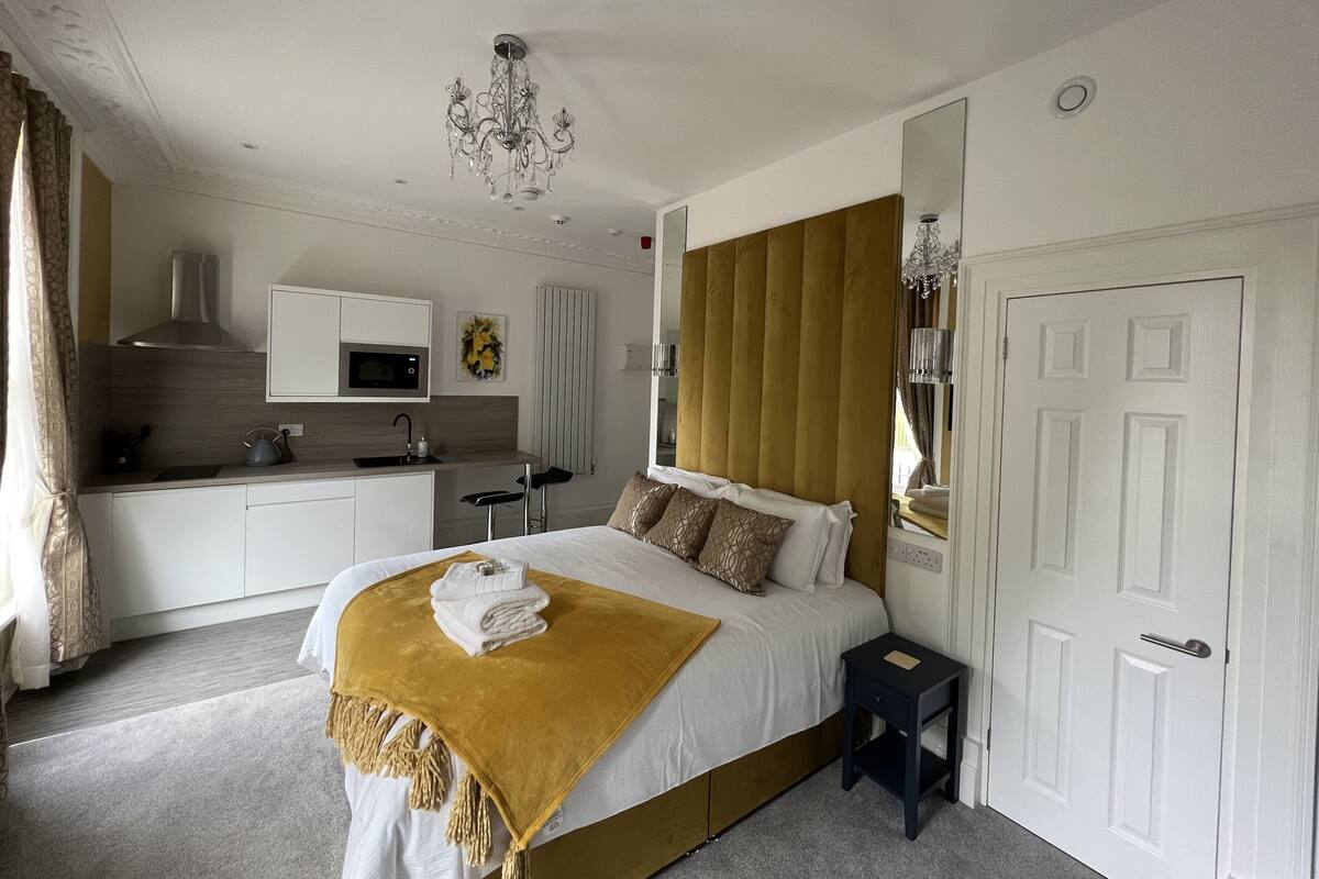 A bedroom with a bed, bedside table, and a small kitchen area with a microwave.