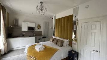 A bedroom with a bed, bedside table, and a small kitchen area with a microwave.