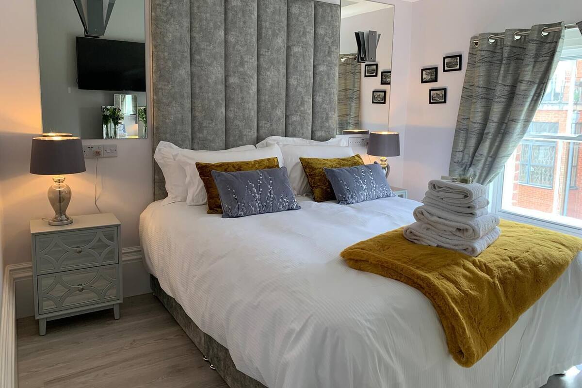 A modern bedroom with a large bed, bedside tables, a flat-screen TV, and a window with curtains.