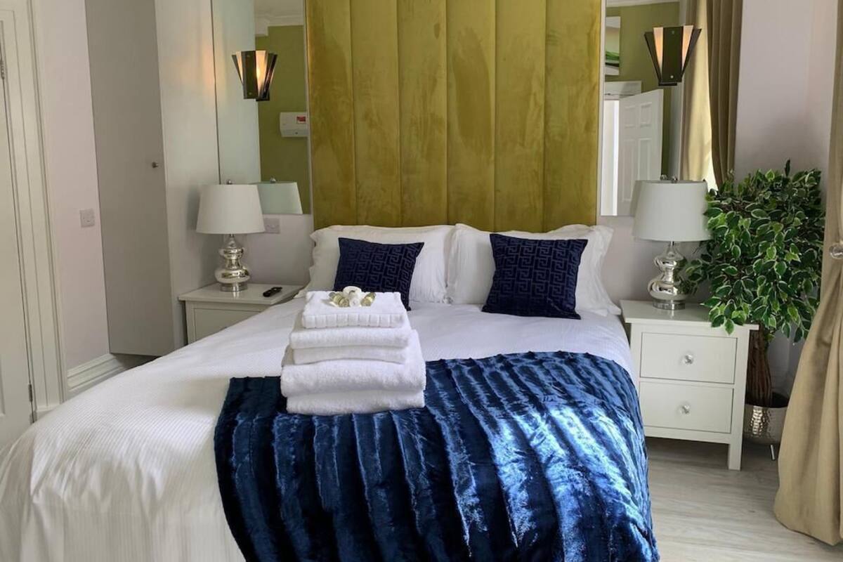 A hotel room with a bed, two bedside tables, a mirror, a plant, and a wardrobe.