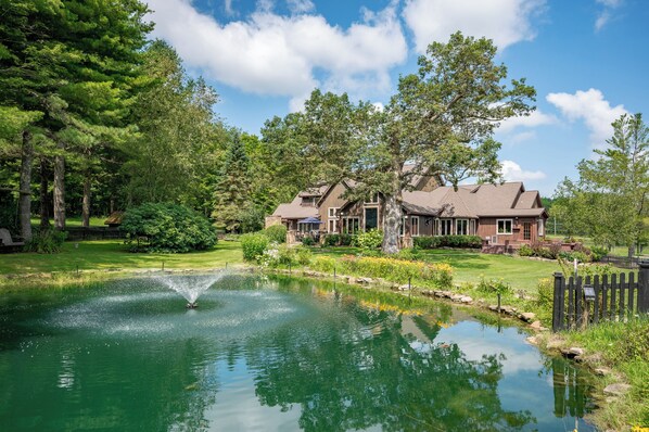 A house with a pond, surrounded by trees and a well-maintained lawn.