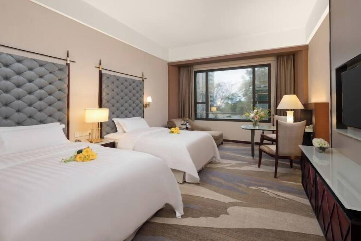 A hotel room with two beds, a desk, a chair, and a TV.