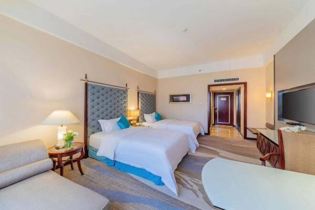 A hotel room with two beds, a TV, a desk, and a chair.