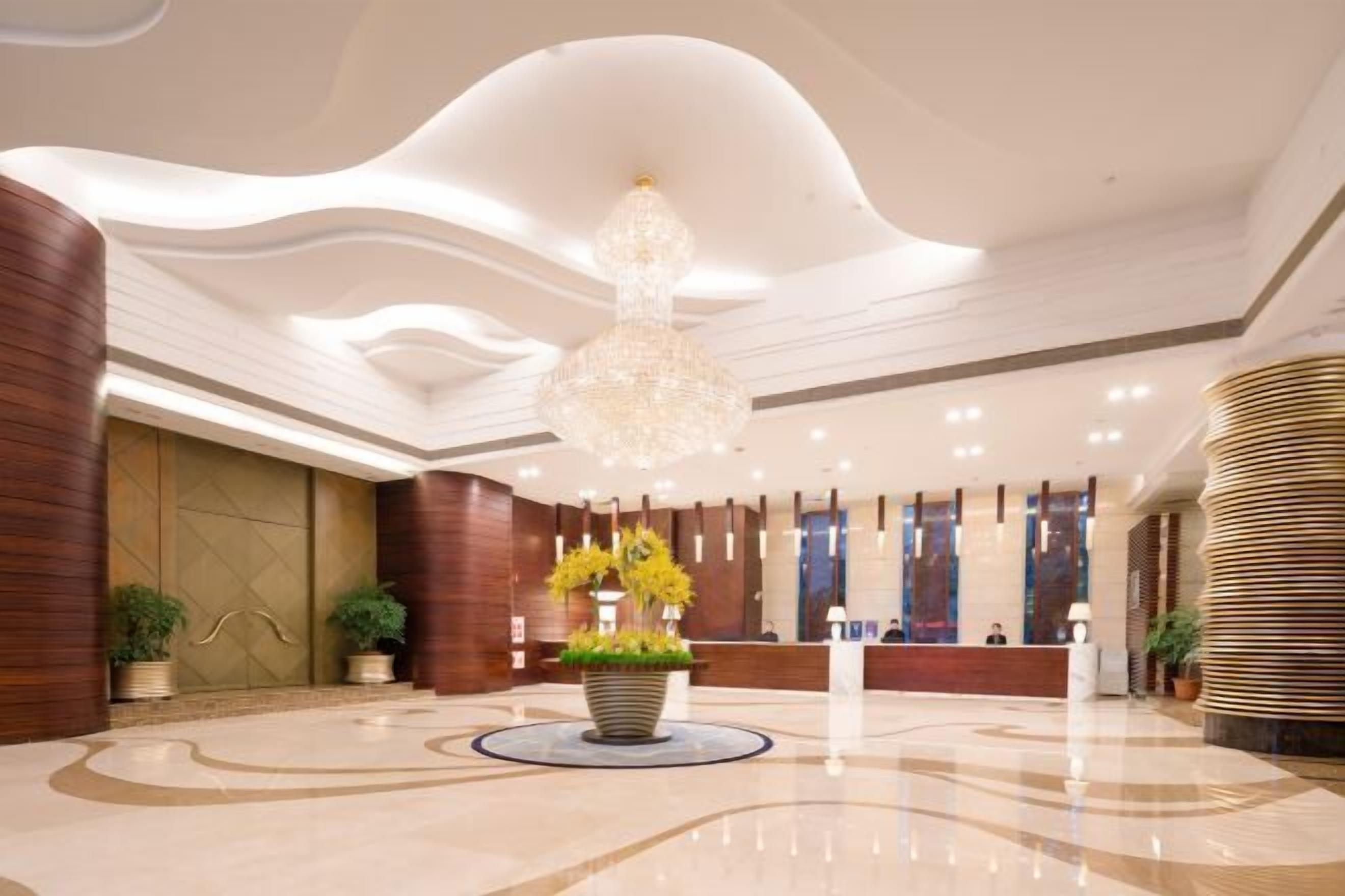 A modern hotel lobby with a central reception desk, a large chandelier, and a circular floor design.