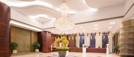 A modern hotel lobby with a central reception desk, a large chandelier, and a circular floor design.