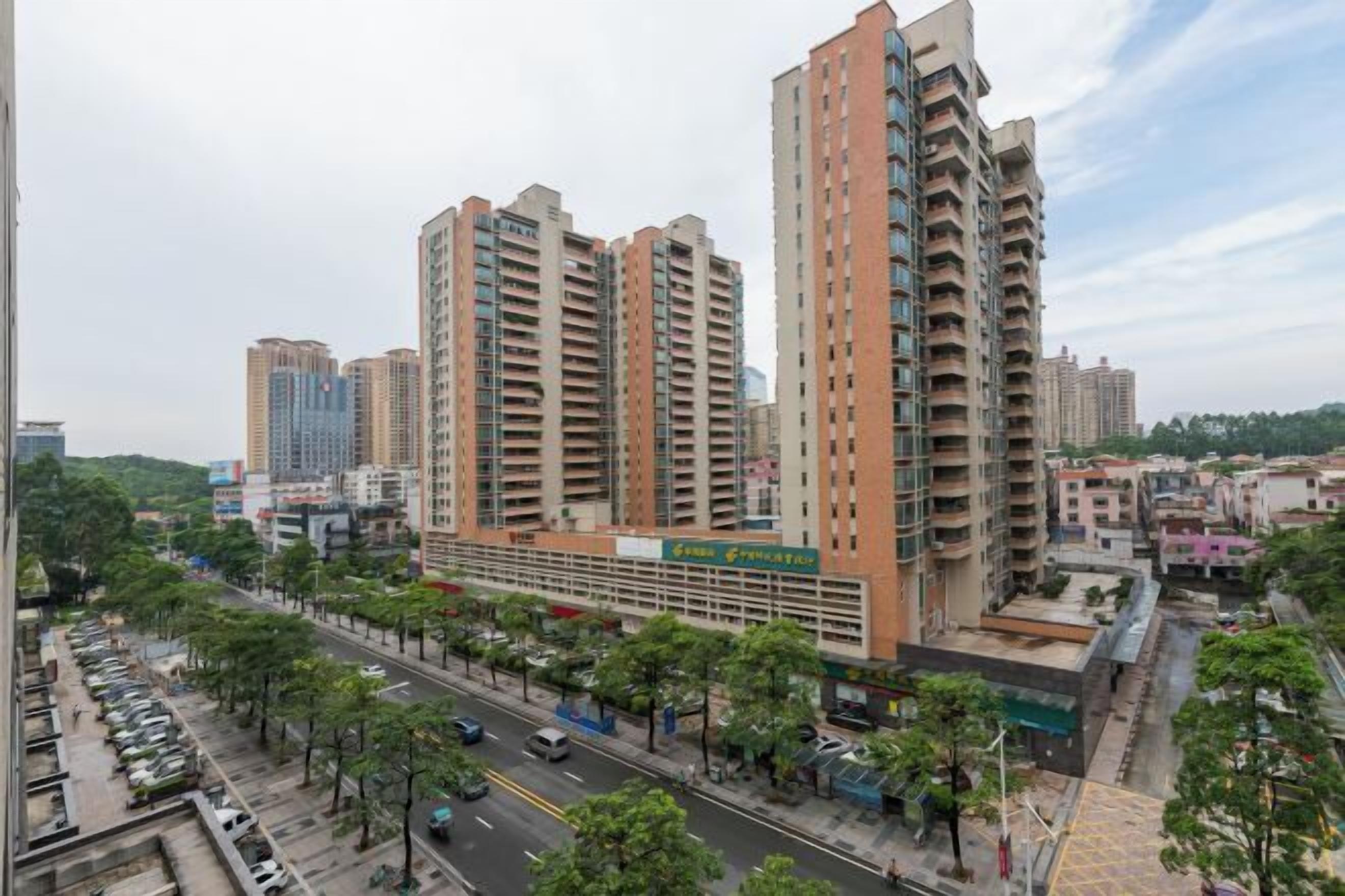 A high-rise residential building with multiple balconies, a commercial ground floor, and a street view with parked cars and trees.