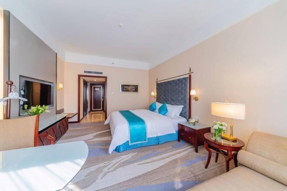 A hotel room with a bed, a desk, a chair, a TV, and a door.