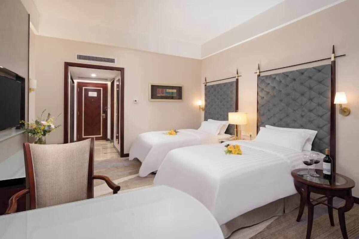 A hotel room with two beds, a TV, a desk, and a chair.