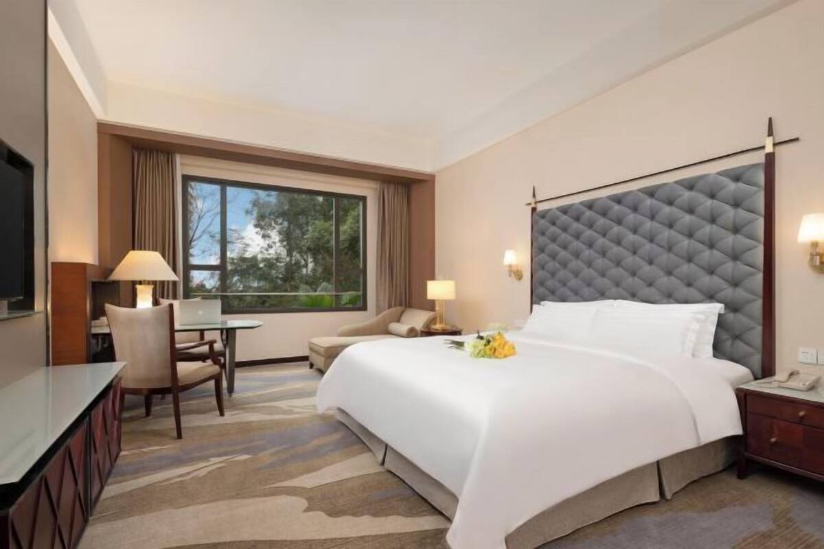 A hotel room with a large bed, a desk, a chair, a TV, and a window with curtains.